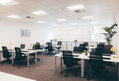 Open-plan office with white desks, black ergonomic chairs, and indoor plants.