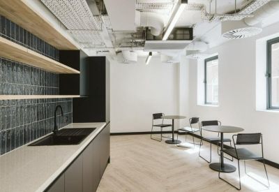 Modern communal kitchen and dining area with chevron wood flooring and exposed ceiling.