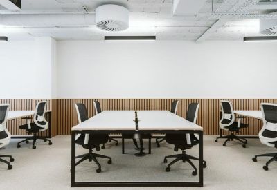 Open-plan office with white desks and black ergonomic chairs against a wood-slat wall.