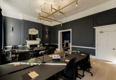 Meeting room with dark grey walls, gold lighting, and a view into an adjacent lounge.