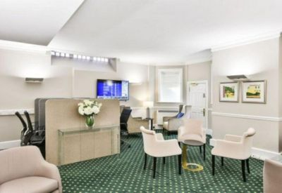 Bright communal lounge area with plush armchairs and a green patterned carpet.