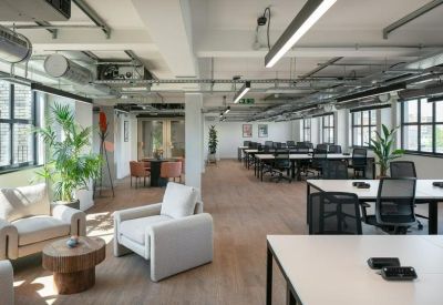 Bright open-plan office featuring rows of white desks and comfortable cream armchairs.
