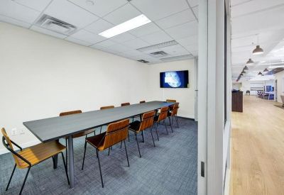 Professional meeting room with a long dark table, wooden chairs, and integrated wall screen.