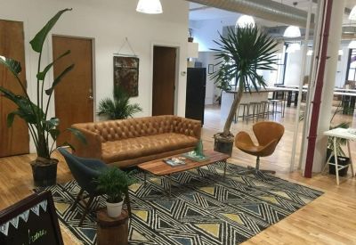 Bright breakout area with a tan tufted sofa, vibrant patterned rug, and large indoor plants.