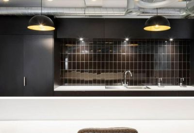 Modern office kitchen area featuring a dark tiled backsplash and sleek white countertops.