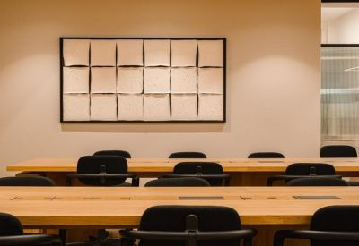 Spacious meeting room with long wooden tables and black chairs beneath a large grid of artwork.