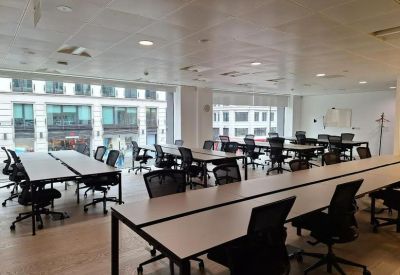 Spacious open-plan office with long rows of desks and floor-to-ceiling windows.