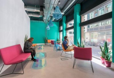 Spacious lounge area featuring teal walls, pink sofas, and large windows with street views.