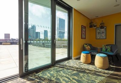 Bright lounge area with yellow walls, colorful armchairs, and views of city skyscrapers.