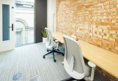 Private office space featuring light wood desks, ergonomic grey chairs, and an exposed brick wall.