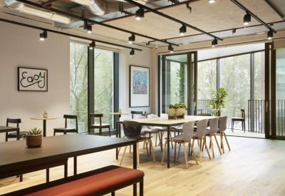 Communal dining area with long wooden tables, track lighting, and a terrace view.