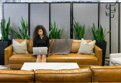 Common area with a tan leather sofa, potted plants, and a person working on a laptop.