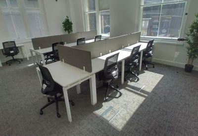Open-plan office space featuring rows of desks with privacy screens and ergonomic black chairs.