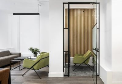 Lounge area with green armchairs and a glass door leading to a private timber-clad booth.