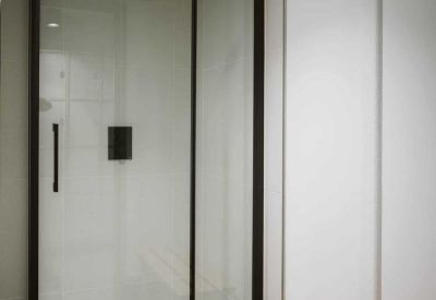 Modern glass-enclosed shower cubicle with black hardware in a clinical white bathroom.