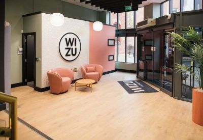 Reception lobby with pink armchairs, wooden floors, and a circular branded logo on the wall.