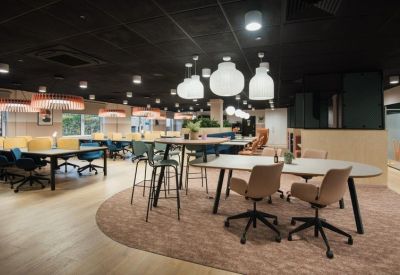 Open-plan coworking space with long tables, ergonomic chairs, and large white pendant lamps.