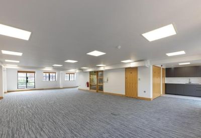 Large open-plan workspace with grey carpeting and modern kitchen cabinetry.