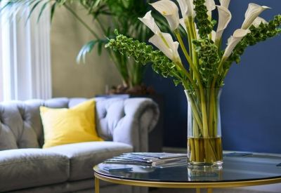 Modern lounge area featuring a grey tufted sofa with a bright yellow cushion and fresh flowers.