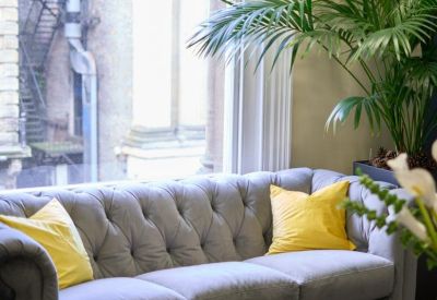 Close-up of a comfortable grey tufted sofa positioned by a large window.