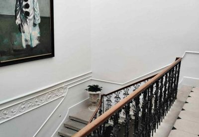Grand staircase featuring intricate wrought iron railings and a large character portrait painting.