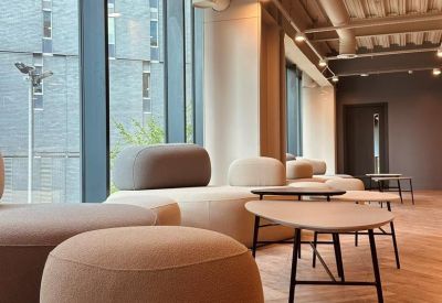 Relaxed lounge area with curved grey sofas and small wooden coffee tables by a window.