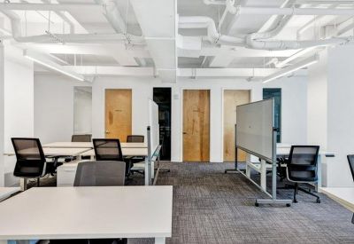 Open-plan office space with white desks, ergonomic chairs, and industrial ceiling pipes.