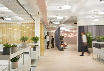 Open-plan coworking space with rows of white desks separated by grey acoustic curtains and leafy plants.
