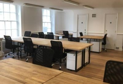 Spacious open-plan office with multiple light wood desks and black ergonomic chairs.