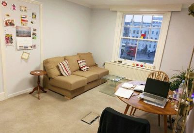 Communal lounge area with a tan sofa, wooden coffee table, and a laptop on a circular desk.