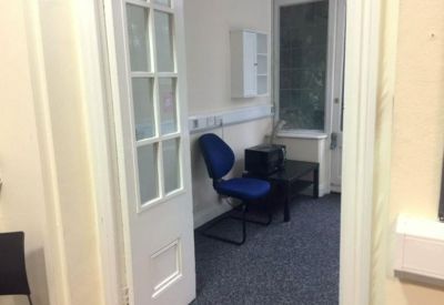 Breakout space with a blue chair, small desk, and a tall window.
