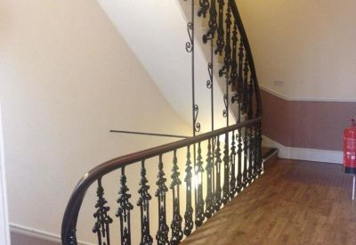 Grand staircase with ornate black wrought iron railings and wooden flooring.