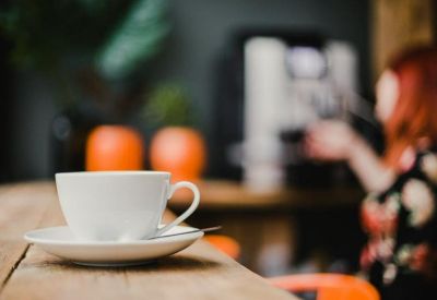 Close-up of a coffee cup on a wooden surface with a soft-focus cafe background.