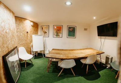 Cozy meeting room featuring a live-edge wooden table, white chairs, and green carpeting.