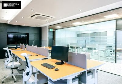 Bright coworking area with wooden desks, ergonomic white chairs, and glass partitions.
