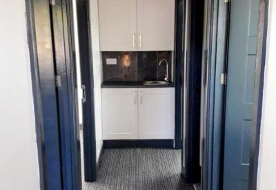Modern communal kitchen area and corridor with dark wood door frames.