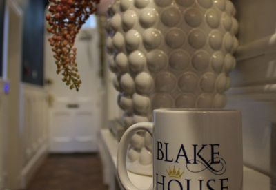 Branded coffee mug in a bright hallway with a white textured vase and floral accents.