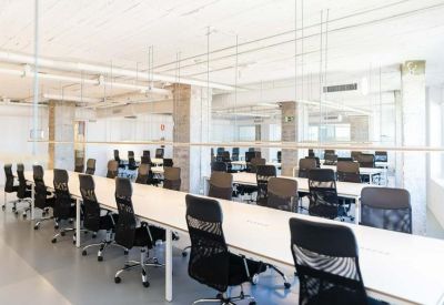 Modern open-plan office with rows of white desks and ergonomic black mesh chairs.