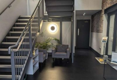 Reception area showing a modern staircase, grey armchairs, and a circular wall light.