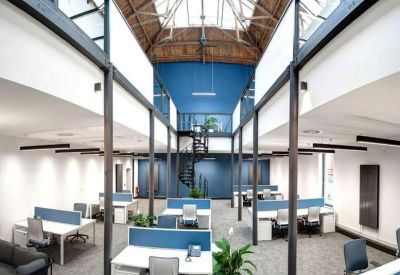 Spacious open-plan office under a skylight with blue partition desks and indoor plants.