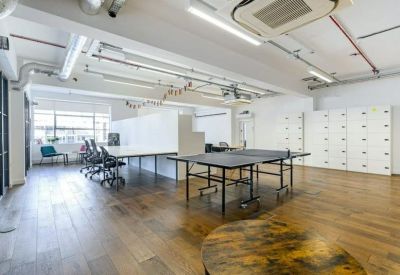 Open-plan office with desks, office chairs, and a ping pong table on hardwood flooring.