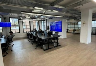 Large open-plan workspace with multiple rows of black desks and industrial ceiling fixtures.