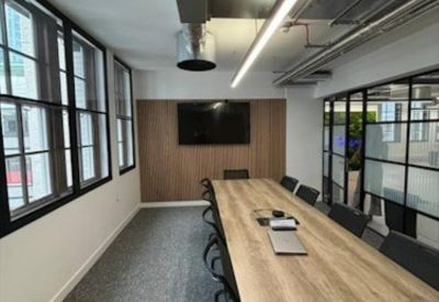 Professional meeting room with a long wooden table, black chairs, and a wall-mounted screen.