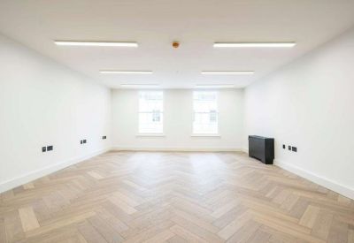 Spacious empty office featuring light herringbone wood floors and bright overhead strip lighting.