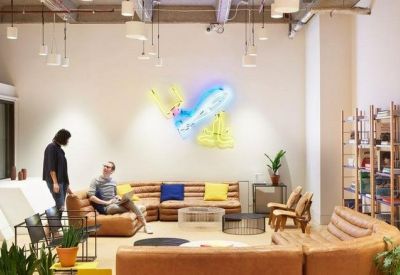 Vibrant communal lounge with tan leather sofas and a neon wall art installation.