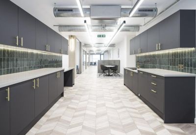 Sleek communal kitchen with dark grey cabinetry, green tiled splashback, and chevron wood-patterned flooring.