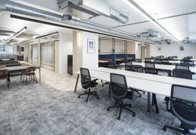 Spacious open-plan office with white desks, ergonomic black chairs, and exposed overhead ducting.