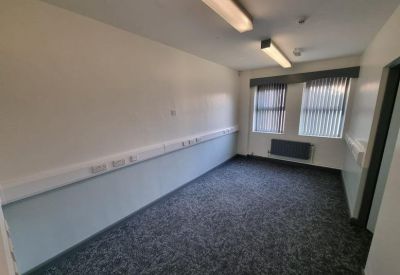 Spacious rectangular office room with white walls and a large window with blinds.