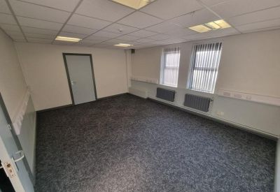 Wide office suite with two windows and grey patterned carpet under bright overhead lights.