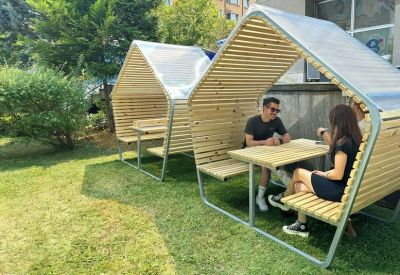 Modern wooden outdoor seating pods with tables on a lush green lawn.